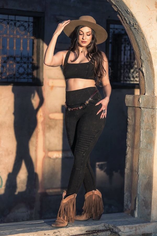 Model tipping her hat to the shadows in Rustique outfit, evoking strength, femininity, and ease of movement.